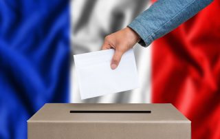 Election in France. The hand of woman putting her vote in the ballot box. French flag on background.