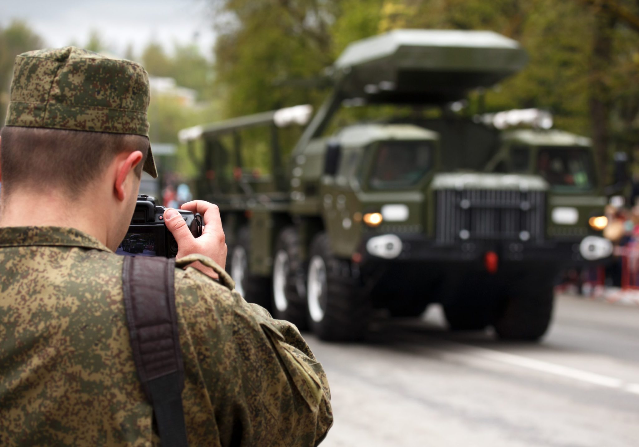 Army journalist photographer. Soldier hold professional camera and takes picture military vehicle