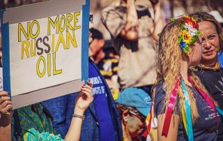 2022_03_05 Tulsa OK USA - Sign at Pro-Ukrainian rally reads No More Russian Oil with blond girl talking to her mother nearby wearing traditional Ukrainian flowers and ribbons in her hair