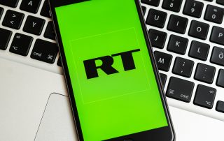 New York / USA - 02/23/2019: Black phone with logo of news media Russia Today (RT) on the screen. RT media icon.