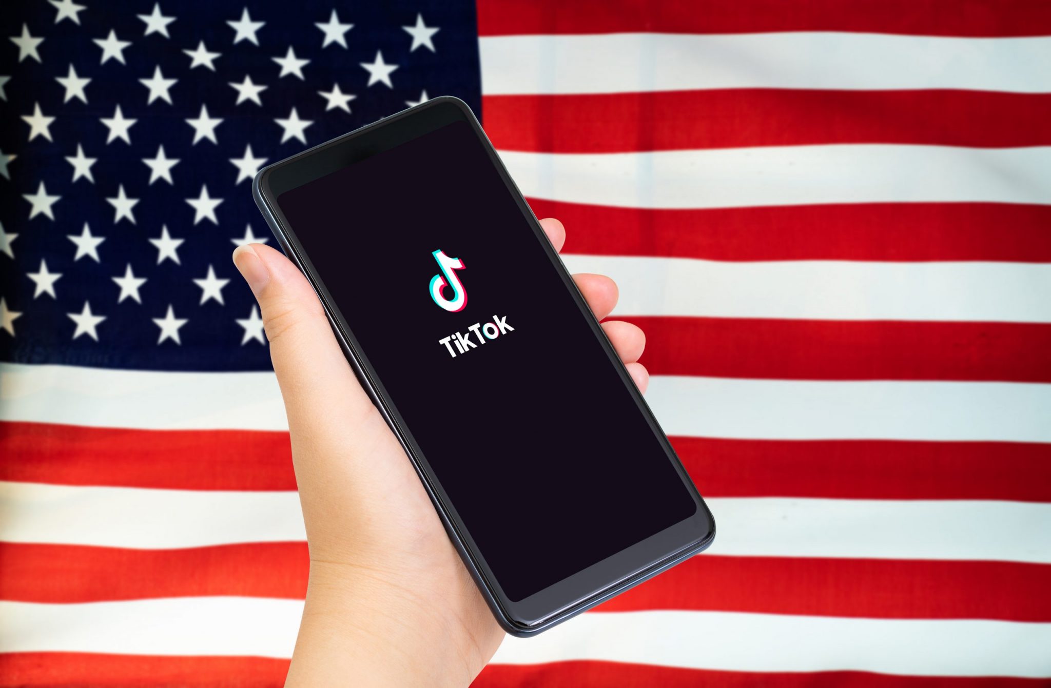 Close up of Hand holding smartphone with TikTok application with US or American flag as background