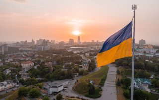 Aerial view of the Ukrainian flag waving in the wind against the city of Kyiv, Ukraine near the famous statue of Motherland at sunset.