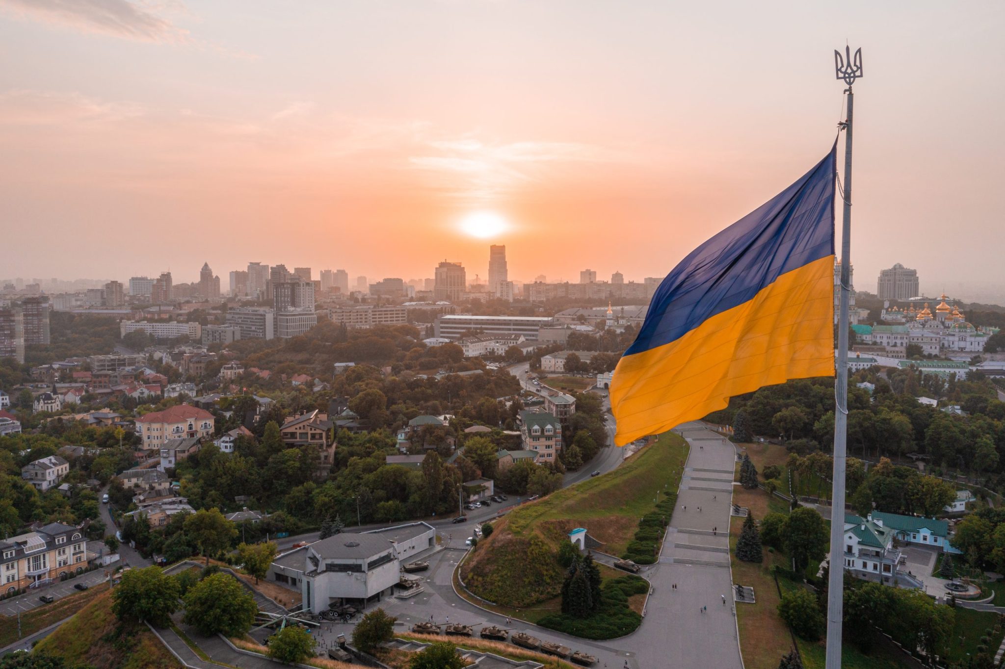 Aerial view of the Ukrainian flag waving in the wind against the city of Kyiv, Ukraine near the famous statue of Motherland at sunset.
